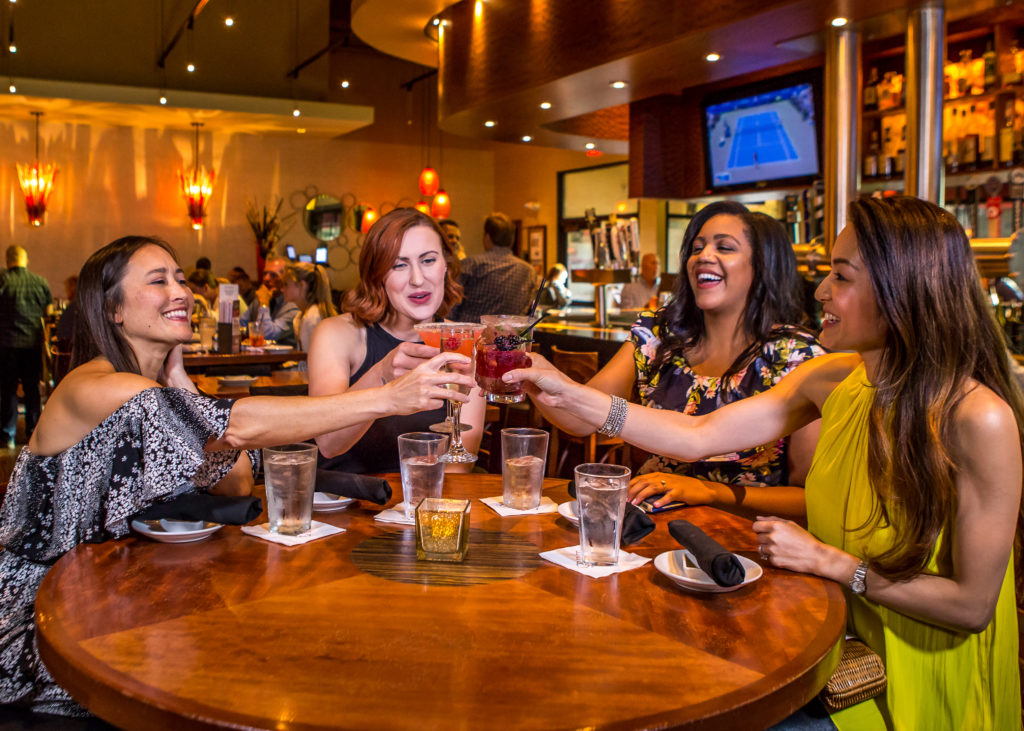 four smiling women with cocktails making a toast