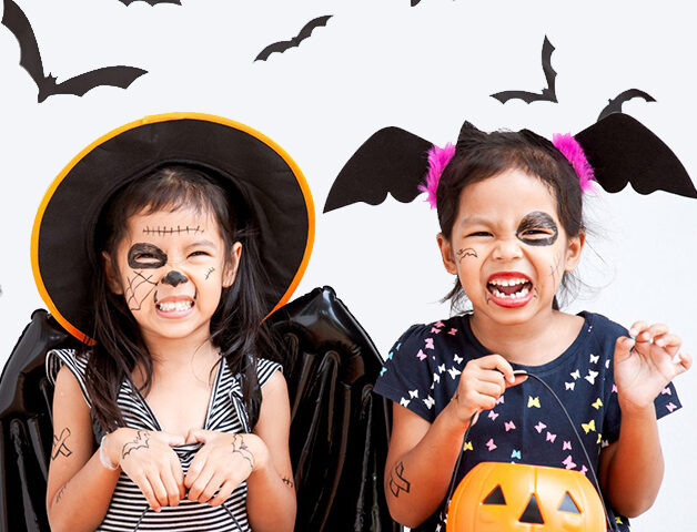 Twin girls dressed up in Halloween costumes holding plastic pumpkin pails with bats flying around them