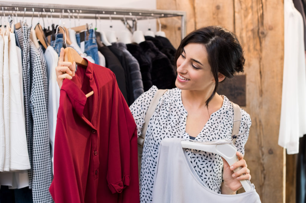 Woman holding two shirts on hangers inside a store while shopping