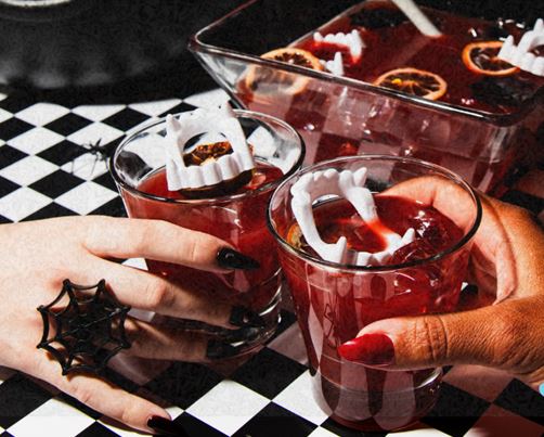 A pair of hands holding two spooky cocktails with vampire teeth floating in them