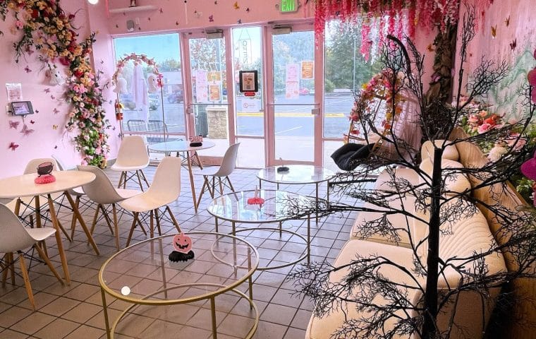 The white and pink interior of MiTea, with white tables and chairs, glass coffee tables and pink and white flowers everywhere.