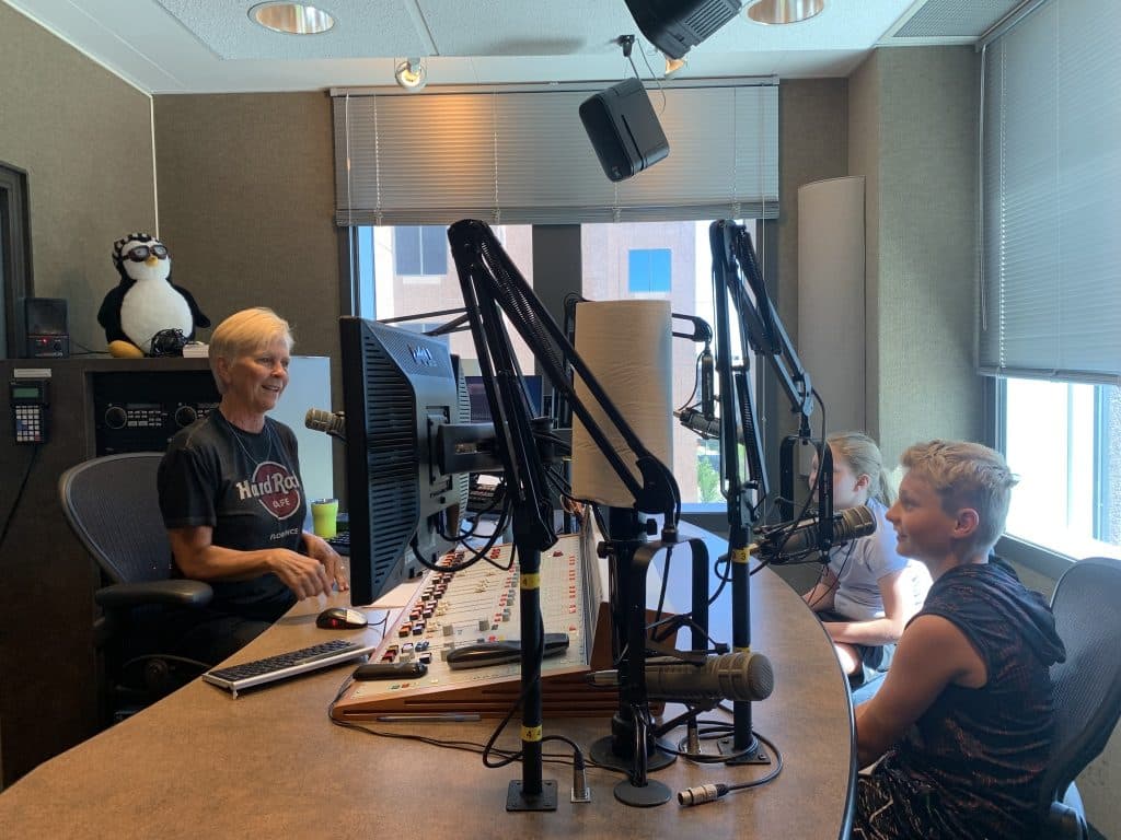 A boy and a girl experimenting with podcasting equipment at the Pavek Museum in St. Louis Park, with an adult guiding them