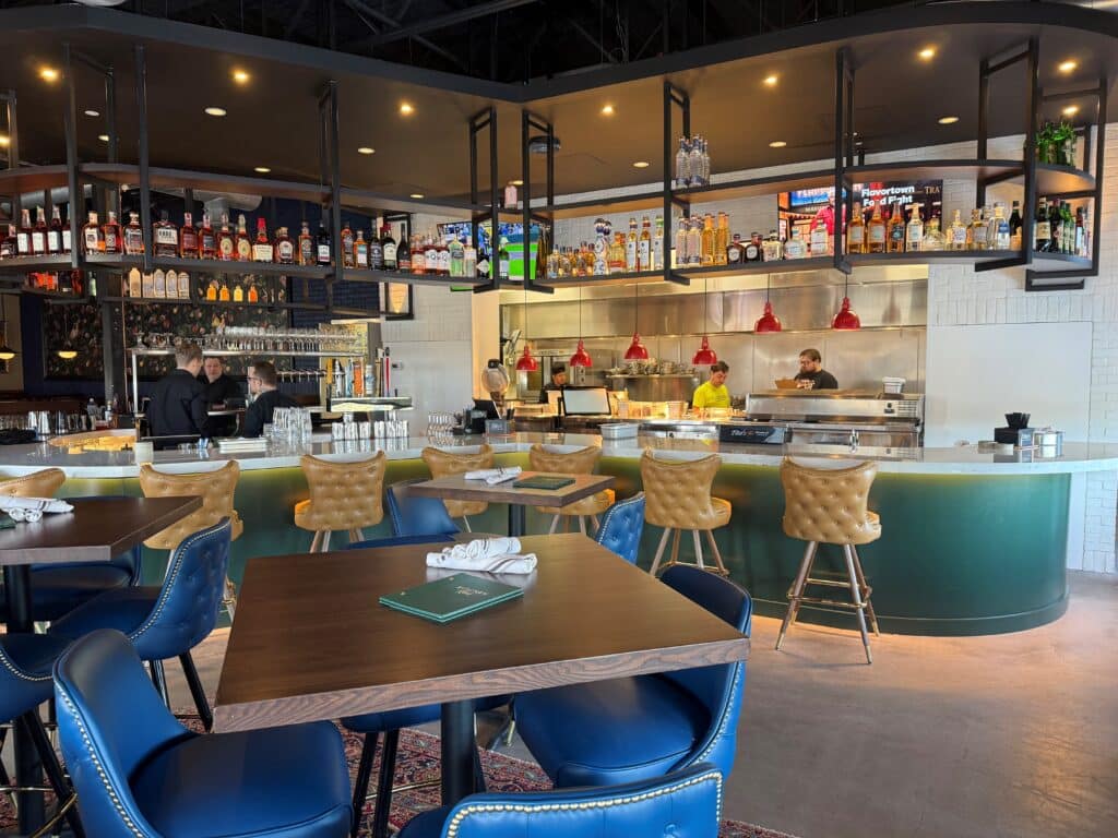 The bar dining area, with low tables with blue leather chairs and golden leather barstools besides a curved bar area at Kitchen and Rail in Golden Valley