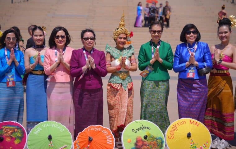 A group of women in colorful Thai clothes standing in a line, with colorful umbrellas on the ground below them that say Songkran Festival
